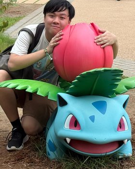 Lucius crouched beside a life-size Ivysaur statue, arms around its flower bulb